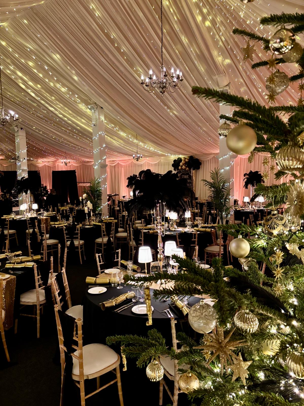 Christmas party tables in black and gold beneath the fairy-lit ceiling at Selden Barns